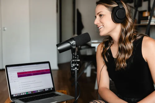 Woman recording a podcast with a microphone and laptop in a home studio.