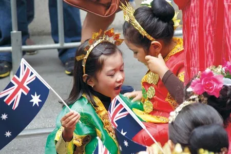 Children in traditional colorful costumes holding Australian flags during a cultural celebration.