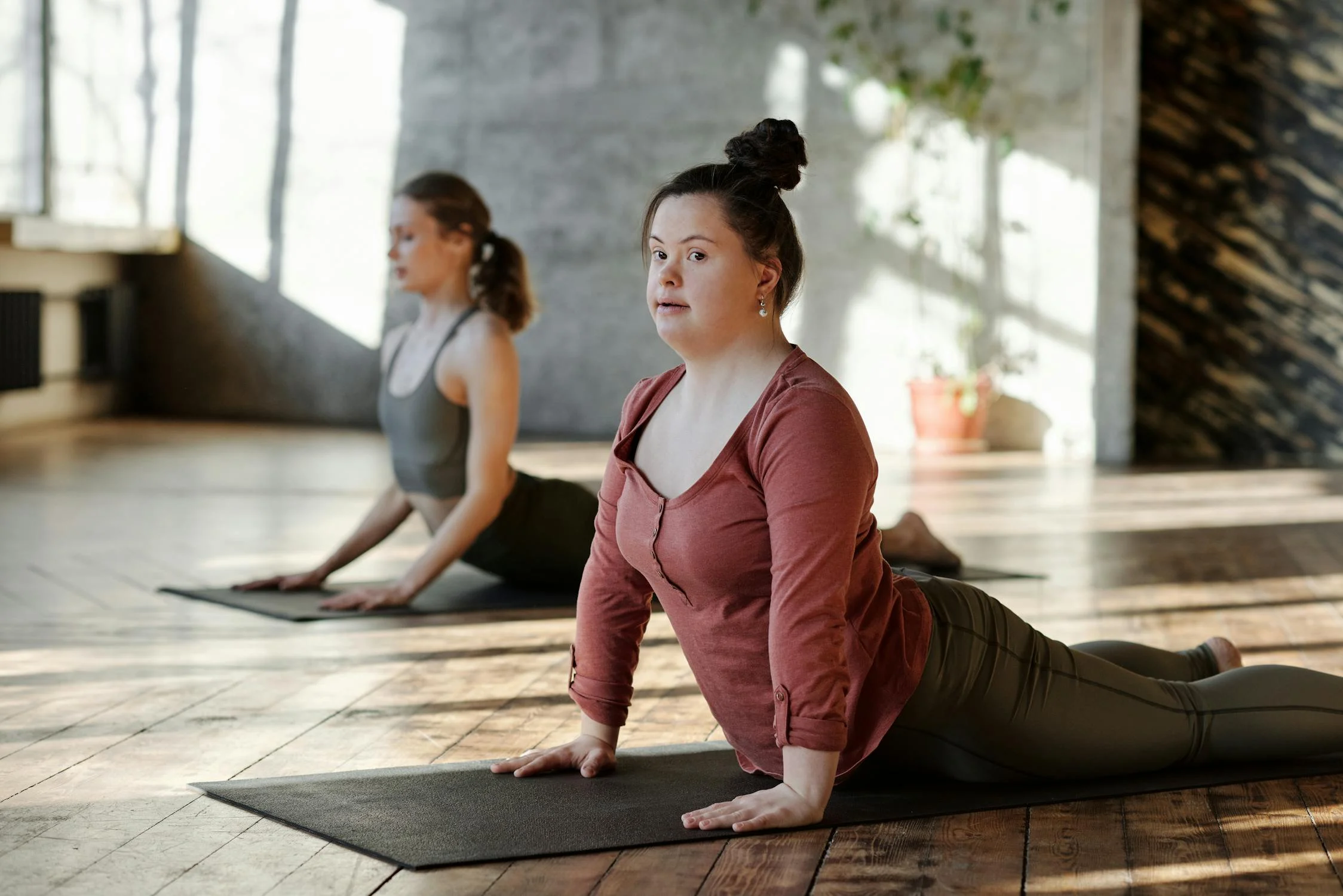 Two women doing upward facing dog pose on yoga mats indoors