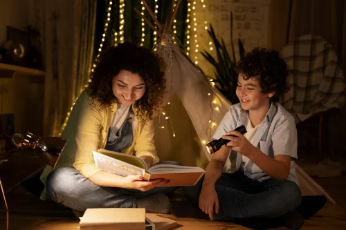 Mother and son reading a book together in a cozy tent with fairy lights.