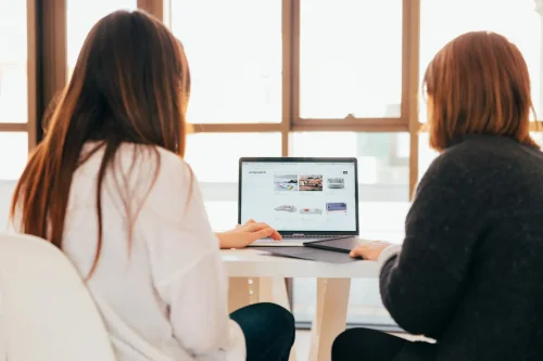 Two women working together on a laptop in a bright office.